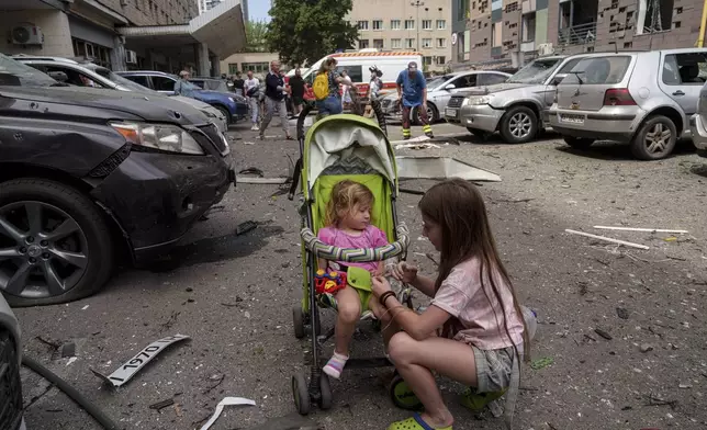 Children wait near the site of Okhmatdyt children’s hospital hit by Russian missiles, in Kyiv, Ukraine, Monday, July 8, 2024. Russian missiles have killed several people and struck a children’s hospital in the Ukrainian capital, Kyiv, authorities say. (AP Photo/Evgeniy Maloletka)