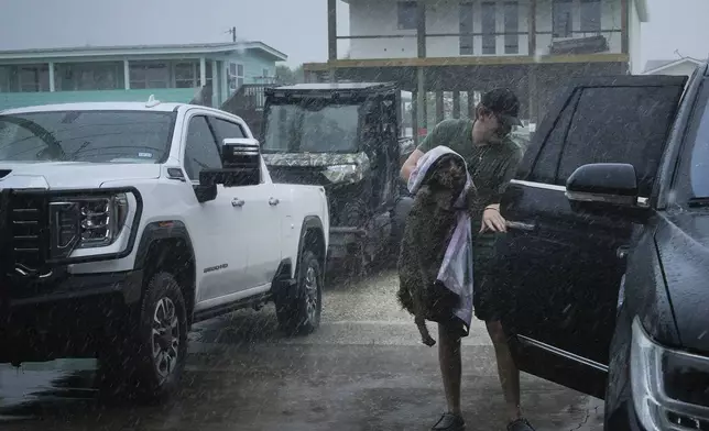 Blake Braun loads his dog Dolly into his family's vehicle as outer bands from Tropical Storm Beryl begin to hit the coast Sunday, July 7, 2024, in Port O'Connor, Texas. (Jon Shapley/Houston Chronicle via AP)