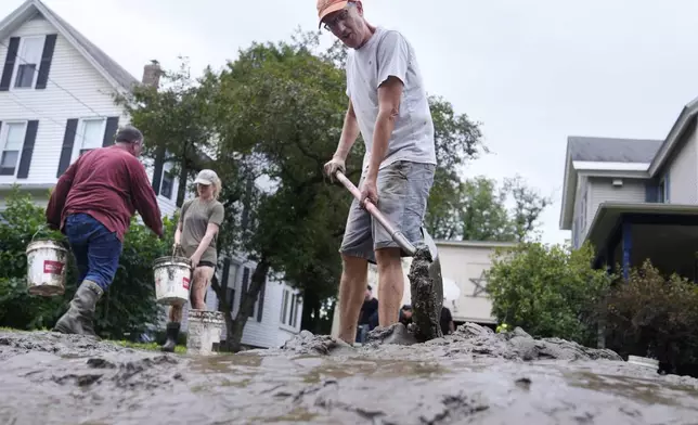 Homeowner Scott Mackie, right, shovels mud away from his home while cleaning up the remnants of Hurricane Beryl, Thursday, July 11, 2024, in Waterbury, Vt. Mackie said his basement was filled with nearly five feet of the muddy mixture, which friends and neighbors are helping to empty. (AP Photo/Charles Krupa)