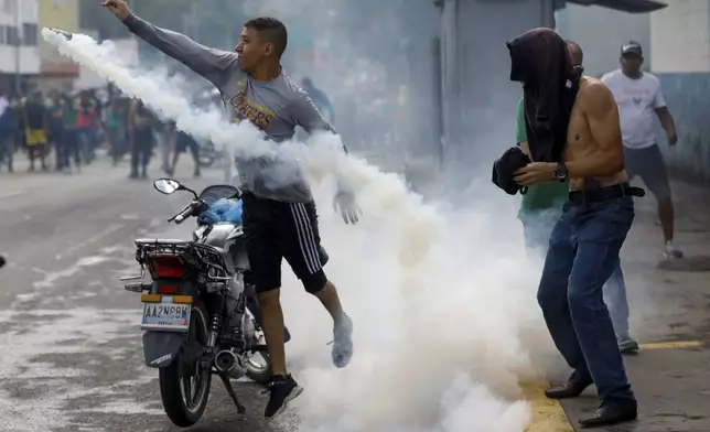 A protester throws a gas canister back at police during demonstrations against the official election results declaring President Nicolas Maduro's reelection, the day after the vote, in Caracas, Venezuela, Monday, July 29, 2024. (AP Photo/Cristian Hernandez)