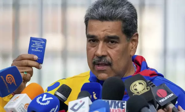 President Nicolas Maduro displays a mini edition of Venezuela's constitution after voting in the presidential elections in Caracas, Venezuela, Sunday, July 28, 2024. Maduro is seeking re-election for a third term. (AP Photo/Fernando Vergara)