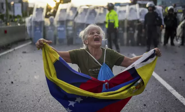 Consuelo Marquez holds a Venezuelan flag in front of police blocking demonstrations against the official election results declaring President Nicolas Maduro's reelection, the day after the vote in Caracas, Venezuela, Monday, July 29, 2024. (AP Photo/Matias Delacroix)