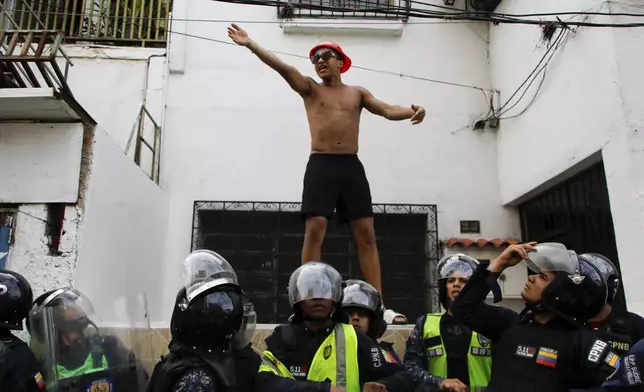 A person stands above police as he joins protests against the official election results declaring President Nicolas Maduro's reelection in Caracas, Venezuela, Monday, July 29, 2024, the day after the vote. (AP Photo/Cristian Hernandez)