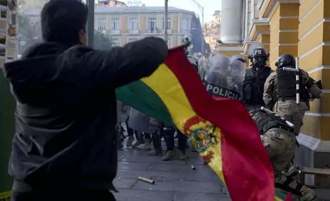 A supporter of President Luis Arce waves a Bolivian flag as soldiers flee from Plaza Murillo, after a failed coup attempt, in La Paz, Bolivia, Wednesday, June 26, 2024. Armored vehicles rammed into the doors of Bolivia's government palace located in Plaza Murillo as Arce said the country faced an attempted coup. (AP Photo/Juan Karita)