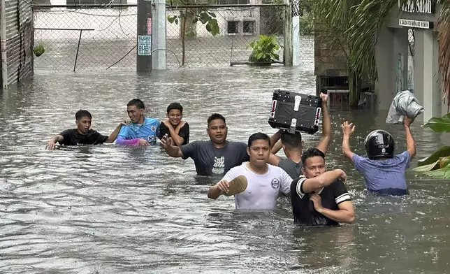 People walk through a street flooded from monsoon rains worsened by offshore typhoon Gaemi on Wednesday, July 24, 2024, in Manila, Philippines. (AP Photo/Joeal Calupitan)