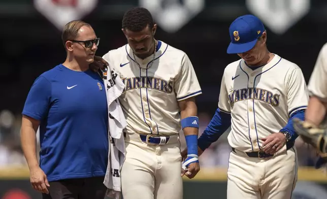 Seattle Mariners centerfielder Julio Rodriguez, center, is helped from the field by manager Scott Servais, right, and a team trainer during the sixth inning of a baseball game against the Houston Astros, Sunday, July 21, 2024, in Seattle. (AP Photo/Stephen Brashear)