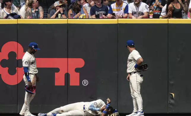 Seattle Mariners Julio Rodriguez, center, lies on the ground between right fielder Victor Robles, left, and left fielder Dylan Moore after crashing into the outfield wall during the eighth inning of a baseball game against the Houston Astros, Sunday, July 21, 2024, in Seattle. (AP Photo/Stephen Brashear)