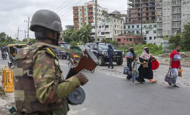 A military person stands guard as a family leaves the city on the fourth day of curfew imposed by the government amidst the countrywide deadly clashes, in Dhaka, Bangladesh, Tuesday, July 23, 2024. Internet and mobile data services are still down despite apparent calm in Bangladesh following a verdict that scaled back a controversial quota system for government jobs after weeks of relentless protests that turned deadly. (AP Photo/Rajib Dhar)