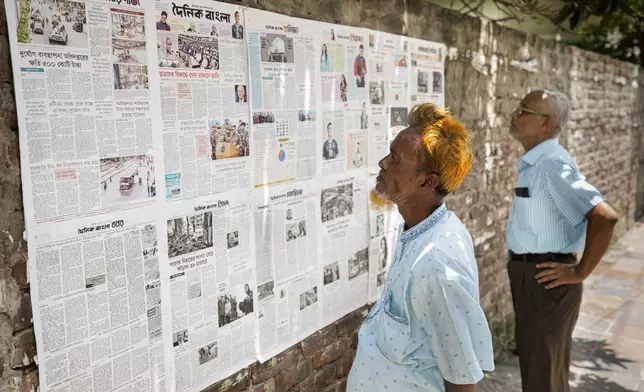 Two men read newspapers pasted by the publishers on a wall by a footpath as Internet blackout continues on the fourth day of curfew imposed by the government amidst the countrywide deadly clashes, in Dhaka, Bangladesh, Tuesday, July 23, 2024. Internet and mobile data services are still down despite apparent calm in Bangladesh following a verdict that scaled back a controversial quota system for government jobs after weeks of relentless protests that turned deadly. (AP Photo/Rajib Dhar)