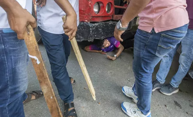 A student hides beneath a vechicle as students clash over quota system at Jahangir Nagar University at Savar outside Dhaka, Bangladesh, Monday, July 15, 2024. Police have fired tear gas and charged with batons overnight during violent clashes between a pro-government student body and student protesters, leaving dozens injured at a leading public university outside Bangladesh's capital over quota system in government jobs, police and students said Tuesday.(AP Photo/Abdul Goni)