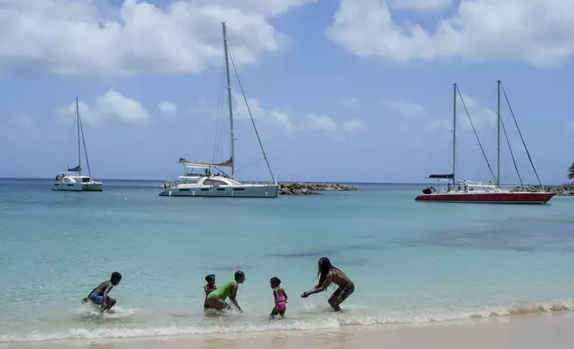 Beachgoers bath as sailboats line up to enter a marina ahead of the the arrival of Hurricane Beryl in Speightstown, Barbados, Sunday, June 30, 2024. (AP Photo/Ricardo Mazalan)