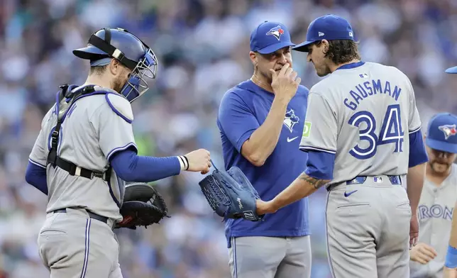 Toronto Blue Jays catcher Danny Jansen, left, hands starting pitcher Kevin Gausman (34) the ball as they have a conference on the mound with pitching coach Pete Walker, seocnd from left, during the fourth inning of a baseball game against the Seattle Mariners, Friday, July 5, 2024, in Seattle. (AP Photo/John Froschauer)