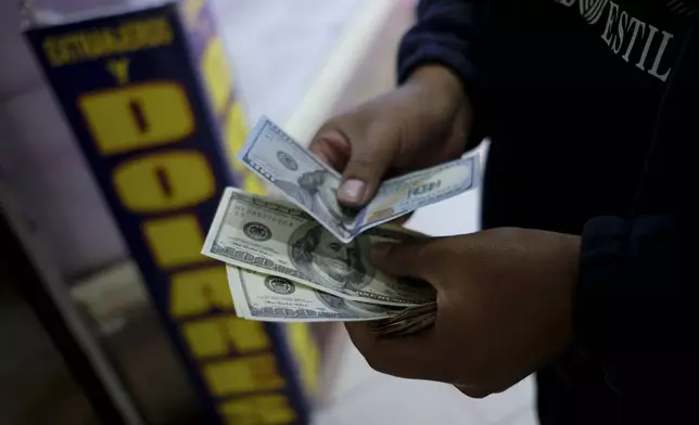 A man holds dollars at a currency exchange shop in La Paz, Bolivia, Friday, June 28, 2024, days after Army troops stormed the government palace in what President Luis Arce called a coup attempt. (AP Photo/Carlos Sanchez)