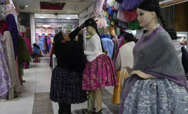 Celia Jaliri places a hat on a mannequin while waiting for customers in her clothing store for Cholitas in La Paz, Bolivia, Saturday, June 29, 2024, days after Army troops stormed the government palace in what President Luis Arce called a coup attempt. (AP Photo/Juan Karita)
