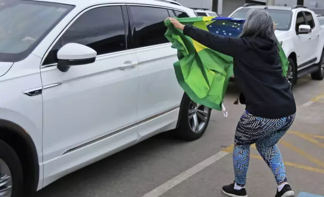 A supporter holds out a Brazilian national flag as the car transporting former Brazilian President Jair Bolsonaro drives by at the international airport in Florianopolis, Santa Catarina state, Brazil, Friday, July 5, 2024. Brazilian police have indicted Bolsonaro for money laundering and criminal association in connection with undeclared diamonds the far-right leader received from Saudi Arabia during his time in office, according to a source with knowledge of the accusations. (AP Photo/Heuler Andrey)