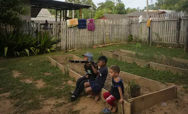 Venezuelan migrant boys play with a toy gun, crafted from square tubing and rope, at a shelter in Assis, Brazil, Thursday, June 20, 2024. The city of Assis Brazil has little to offer to immigrants but the wooden shelter and a school gymnasium where the men can sleep. (AP Photo/Martin Mejia)