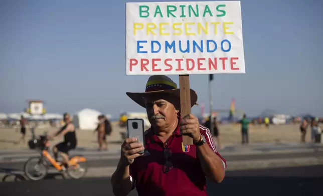 A Venezuelan holds a sign that reads in Spanish: "Barinas present. Edmundo President," during a gathering of Venezuelans in support of opposition presidential candidate Edmundo Gonzalez on the day of the presidential election in Venezuela, on Copacabana beach in Rio de Janeiro, Brazil, Sunday, July 28, 2024. (AP Photo/Bruna Prado)