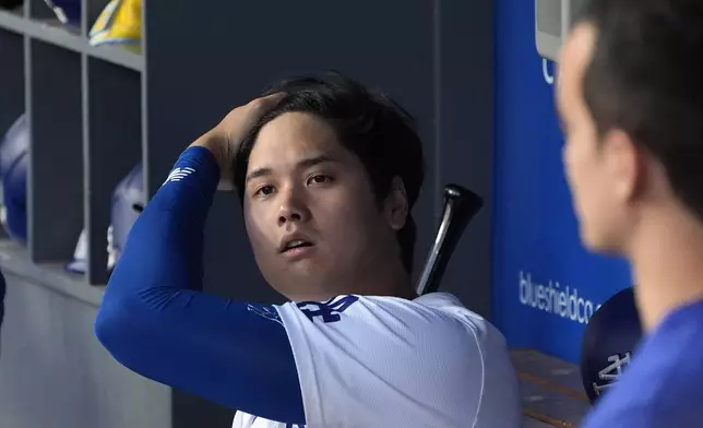 Los Angeles Dodgers' Shohei Ohtani, left, runs his fingers through his hair in the dugout as his interpreter Will Ireton stands by prior to a baseball game against the Milwaukee Brewers Friday, July 5, 2024, in Los Angeles. (AP Photo/Mark J. Terrill)