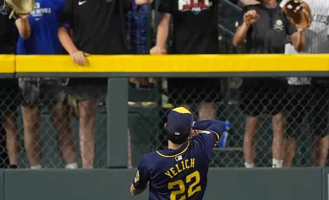 Milwaukee Brewers left fielder Christian Yelich tosses a ball to fans in the eighth inning of a baseball game against the Colorado Rockies, Wednesday, July 3, 2024, in Denver. (AP Photo/David Zalubowski)