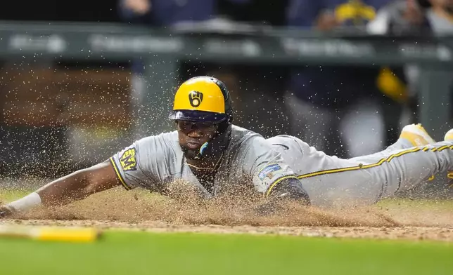Milwaukee Brewers' Andruw Monasterio slides across home plate to score the tying run on a sacrifice fly hit by Willy Adames off Colorado Rockies relief pitcher Nick Mears in the ninth inning of a baseball game Tuesday, July 2, 2024, in Denver. (AP Photo/David Zalubowski)