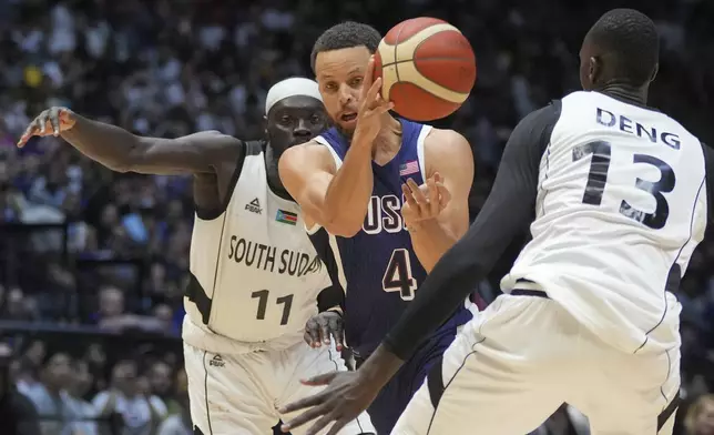 United States' guard Stephen Curry, centre, passes the ball as South Sudan's forward Majok Deng, right, and South Sudan's guard Marial Shayok defend during an exhibition basketball game between the United States and South Sudan, at the o2 Arena in London, Saturday, July 20, 2024. (AP Photo/Kin Cheung)