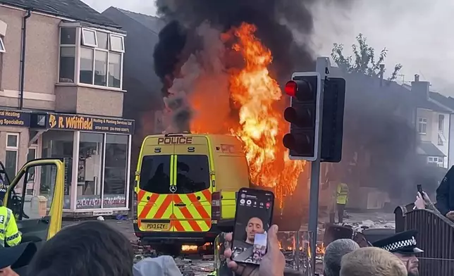 A police van buns as and unruly crowd clashed with police, Tuesday, July 30, 2024, in Southport, northwest England, near where three girls were stabbed to death in a dance class the day before. The violence erupted shortly after a peaceful vigil was attended by hundreds in the center of Southport to mourn the 13 victims of the stabbings, including seven still in critical condition. (Richard McCarthy/PA via AP)