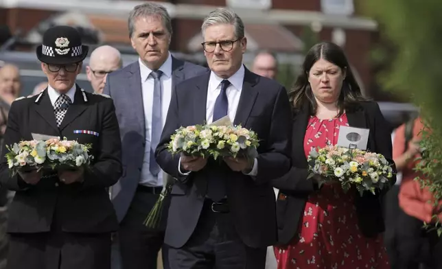 British Prime Minister Keir Starmer, center, carries a floral tribute near the scene in Hart Street, where three children died and eight were injured in a knife attack during a Taylor Swift event at a dance school on Monday, in Southport, England, Tuesday, July 30, 2024. (James Speakman/PA via AP)