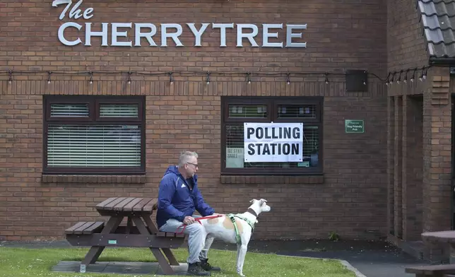 A voter waits with his dog after casting his vote at the Cherry Tree public house which is being used a polling station in Urpeth, County Durham, northern England, Thursday, July 4, 2024. Britain goes to the polls Thursday after Prime Minister Rishi Sunak called a general election. (AP Photo/Scott Heppell)