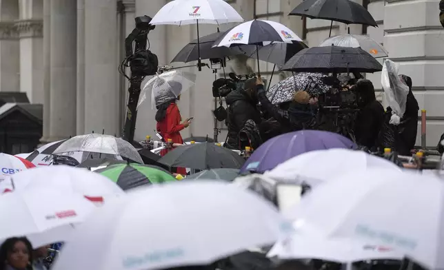 Members of the media shelter under umbrellas as they wait for the arrival of Britain's Prime Minister Rishi Sunak and then Labour leader Keir Starmer outside 10 Downing Street in London, Friday, July 5, 2024. Britain's Labour Party swept to power Friday after more than a decade in opposition, as a jaded electorate handed the party a landslide victory — but also a mammoth task of reinvigorating a stagnant economy and dispirited nation. (AP Photo/Vadim Ghirda)