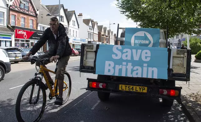 A cyclist passes a van with advertising for the Reform UK Party in Clacton On Sea, England, Thursday, July 4, 2024. Voters in the U.K. are casting their ballots in a national election to choose the 650 lawmakers who will sit in Parliament for the next five years. Outgoing Prime Minister Rishi Sunak surprised his own party on May 22 when he called the election. (AP Photo/Thomas Krych)
