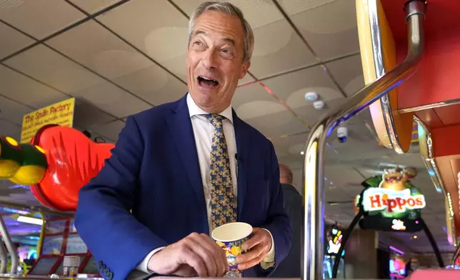 FILE - Britain's Nigel Farage, Reform UK party leader plays on a game in an amusement arcade holds out some coins whilst spending time with supporters in Clacton-On-Sea, Essex, England Friday, June 21, 2024. The United Kingdom will hold its first national election in almost five years on Thursday, with opinion polls suggesting that Prime Minister Rishi Sunak’s Conservative Party will be punished for failing to deliver on promises made during 14 years in power. (AP Photo/Kirsty Wigglesworth, File)