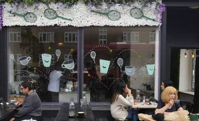 People sit outside at a coffee shop decorated with tennis raquets, in Southfields near the All England Lawn Tennis and Croquet Club in Wimbledon, London, Friday, June 28, 2024. The Wimbledon Championships begin on July 1. (AP Photo/Kirsty Wigglesworth)
