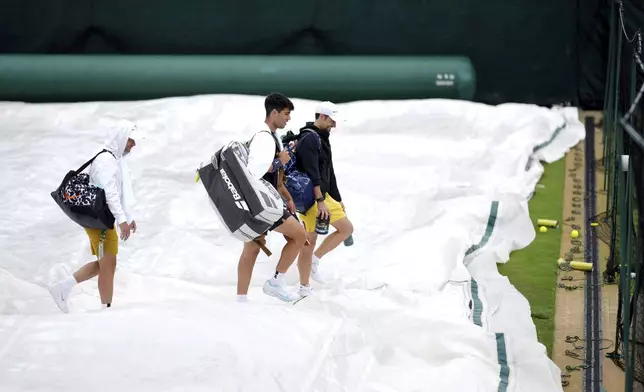 Spain's Carlos Alcaraz, centre and his team walk over rain covers, at the All England Lawn Tennis and Croquet Club in Wimbledon, London, Sunday, June 30, 2024. The Wimbledon Championships begin on July 1. (John Walton/PA via AP)