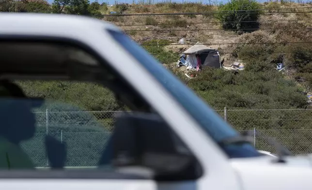 A commuter drives past a homeless encampment on the side of the CA-105 freeway on Friday, July 26, 2024, in Los Angeles. (AP Photo/Damian Dovarganes)