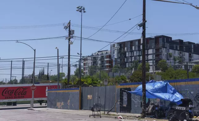 A homeless encampment sits across the street of a newly built apartment building being offered for leasing near the CA-110 freeway on Friday, July 26, 2024, in Los Angeles. (AP Photo/Damian Dovarganes)