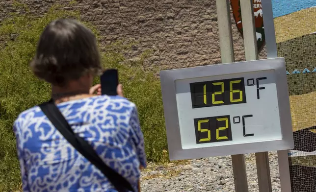 A woman takes a photo of a thermostat reading 126 degrees Fahrenheit and 52 degrees Celsius at the Furnace Creak Visitors Center in Death Valley National Park, Calif., Sunday, July 7, 2024. Forecasters say a heat wave could break previous records across the U.S. including at Death Valley. (AP Photo/Ty ONeil)