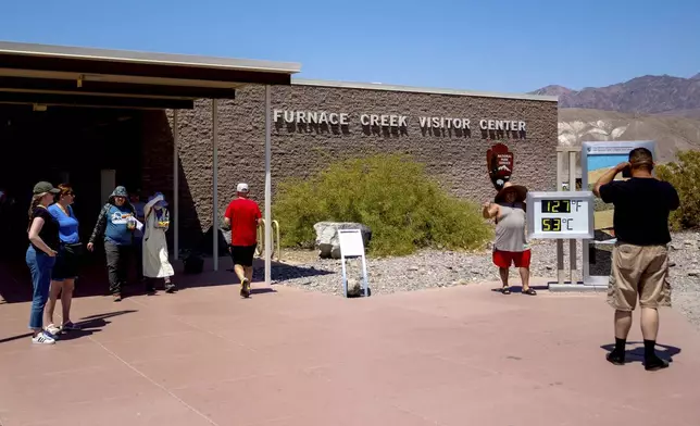 Tourists take photographs with the thermometer at the Furnace Creek Visitor Center during a dangerous heat wave, Tuesday, July 9, 2024, in Death Valley, Calif. The thermostat is imprecise, registering the temperature anywhere from 1 to 5 degrees Fahrenheit higher than more precise instruments and providing a more impressive reading for pictures. (AP Photo/Ty ONeil)