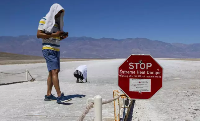 Two people cover themselves in white towels as they walk around Badwater Basin in Death Valley National Park, Calif., Sunday, July 7, 2024. Forecasters say a heat wave could break previous records across the U.S. (AP Photo/Ty ONeil)