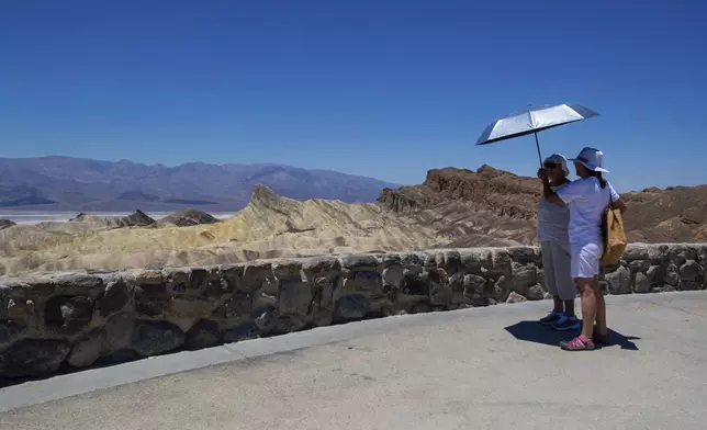 Alina Rogers, right, from Pennsylvania, holds an umbrella up for a family member visiting from Hungary at Zabriskie Point in Death Valley National Park, Calif., Sunday, July 7, 2024. Forecasters say a heat wave could break previous records across the U.S. including at Death Valley. (AP Photo/Ty ONeil)