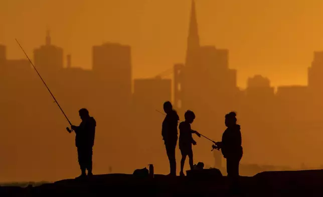 With the San Francisco skyline behind them, people fish off a jetty Monday, July 1, 2024, in Alameda, Calif. An extended heatwave predicted to blanket Northern California has resulted in red flag fire warnings and the possibility of power shutoffs beginning Tuesday. (AP Photo/Noah Berger)