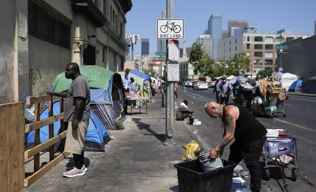 Two men work and stand on a sidewalk on Skid Row, Thursday, July 25, 2024, in Los Angeles. California Gov. Gavin Newsom issued an executive order Thursday to direct state agencies on how to remove homeless encampments, a month after a Supreme Court ruling allowing cities to enforce bans on sleeping outside in public spaces. (AP Photo/Jae C. Hong)