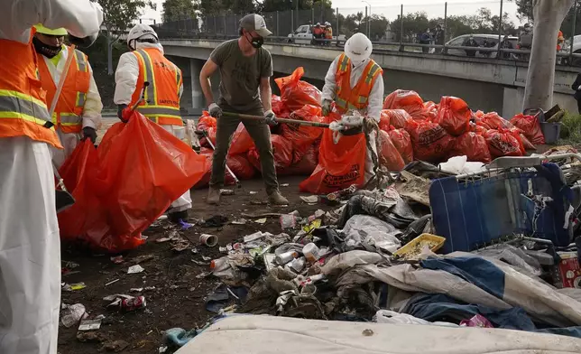 FILE - California Gov. Gavin Newsom, center, helps clean a homeless encampment alongside a freeway on Jan. 12, 2022, in San Diego. Newsom issued an executive order Thursday, July 25, 2024, for the removal of homeless encampments in the state. (AP Photo/Gregory Bull, File)