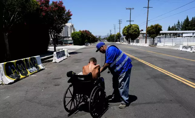 Ruben Rodriguez with Hope the Mission gives gives water to a homeless man in a wheelchair near the 405 Freeway in the Van Nuys section of Los Angeles on Friday, July 26, 2024. California Gov. Gavin Newsom has issued an executive order directing state agencies "to move urgently to address dangerous" homeless encampments and clear them from state land while giving city and local leaders a push to do the same. (AP Photo/Jae C. Hong)