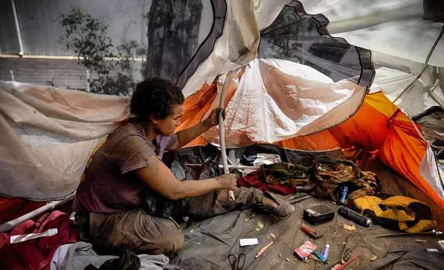 Suffering from homelessness Esca Guernon fixes her tent that's set up at an encampment next to the 405 Freeway in the Van Nuys section of Los Angeles on Friday, July 26, 2024, in Los Angeles. California Gov. Gavin Newsom has issued an executive order directing state agencies "to move urgently to address dangerous" homeless encampments and clear them from state land while giving city and local leaders a push to do the same. (AP Photo/Jae C. Hong)