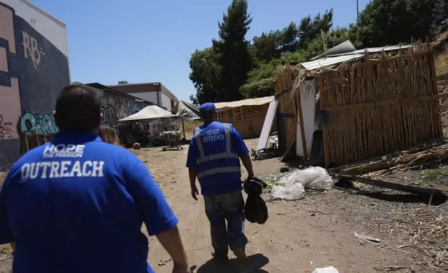 Workers with Hope the Mission walk past a homeless encampment next to the 405 Freeway in the Van Nuys section of Los Angeles on Friday, July 26, 2024, in Los Angeles. California Gov. Gavin Newsom has issued an executive order directing state agencies "to move urgently to address dangerous" homeless encampments and clear them from state land while giving city and local leaders a push to do the same. (AP Photo/Jae C. Hong)