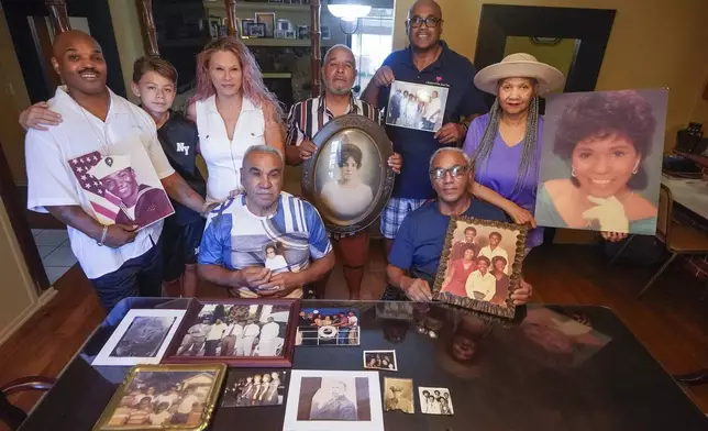 Descendants of Nelson Bell, brothers Milford Fonza, front left, and Elmer Fonza, front right, surrounded by extended family members, show their ancestors' pictures in Glendora, Calif., on Friday, Sept. 8, 2023. Family members standing from left: Trent Mure, with son Armani Mure, and his wife Tami Mure, William Woolery, Louie Hobbs and Carolyn Fonza. (AP Photo/Damian Dovarganes)