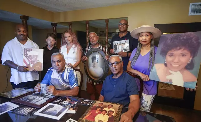 Descendants of Nelson Bell, brothers Milford Fonza, front left, and Elmer Fonza, front right, surrounded by extended family members, show their ancestors' pictures in Glendora, Calif., on Friday, Sept. 8, 2023. Family members standing from left: Trent Mure, with son Armani Mure, and his wife Tami Mure, William Woolery, Louie Hobbs and Carolyn Fonza. (AP Photo/Damian Dovarganes)