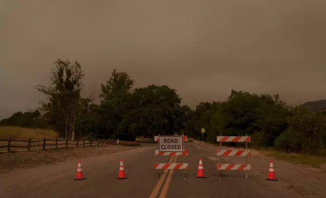 Signs and traffic cones block a road to Sycamore Valley Ranch, formerly called Neverland Ranch when it was owned by Michael Jackson, as firefighters work against the advancing Lake Fire in Los Olivos, Calif., Saturday, July 6, 2024. (AP Photo/Eric Thayer)