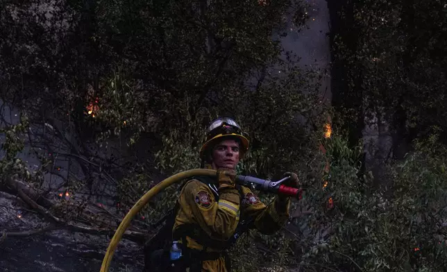 Rocco Olhiser, a firefighter with the Colusa Fire Department, carries a hose while battling the Thompson fire in Oroville, Tuesday, July 2, 2024. (Stephen Lam/San Francisco Chronicle via AP)
