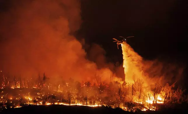 A night flying helicopter drops water on flames as the Thompson Fire burns, Tuesday, July 2, 2024, in Oroville, Calif. (AP Photo/Ethan Swope)